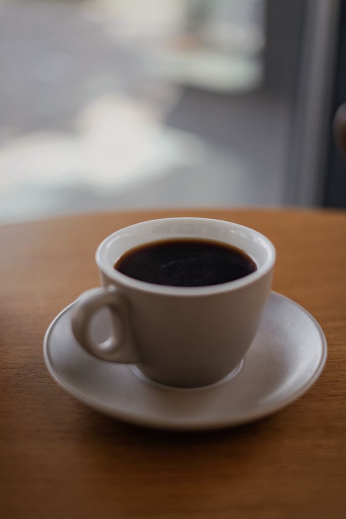 Services A close-up shot of espresso coffee in a white ceramic cup with a saucer on a wooden table.