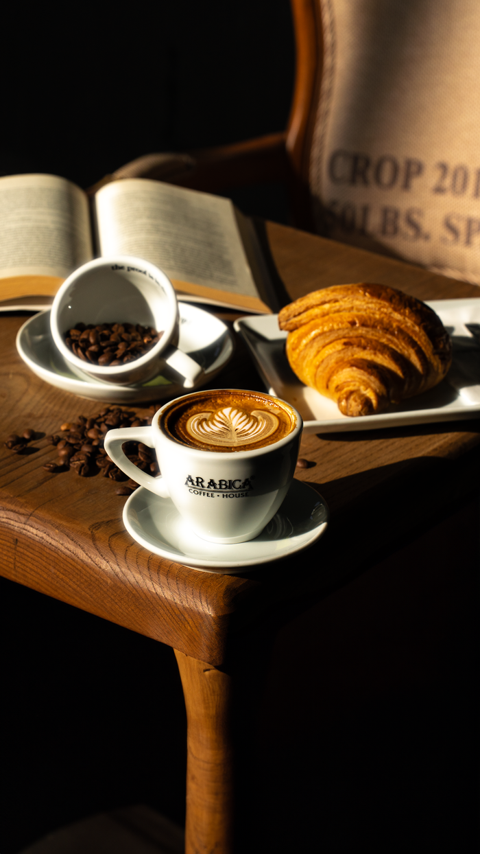 Home Enjoy a morning coffee with latte art alongside a fresh croissant in a cozy setting.