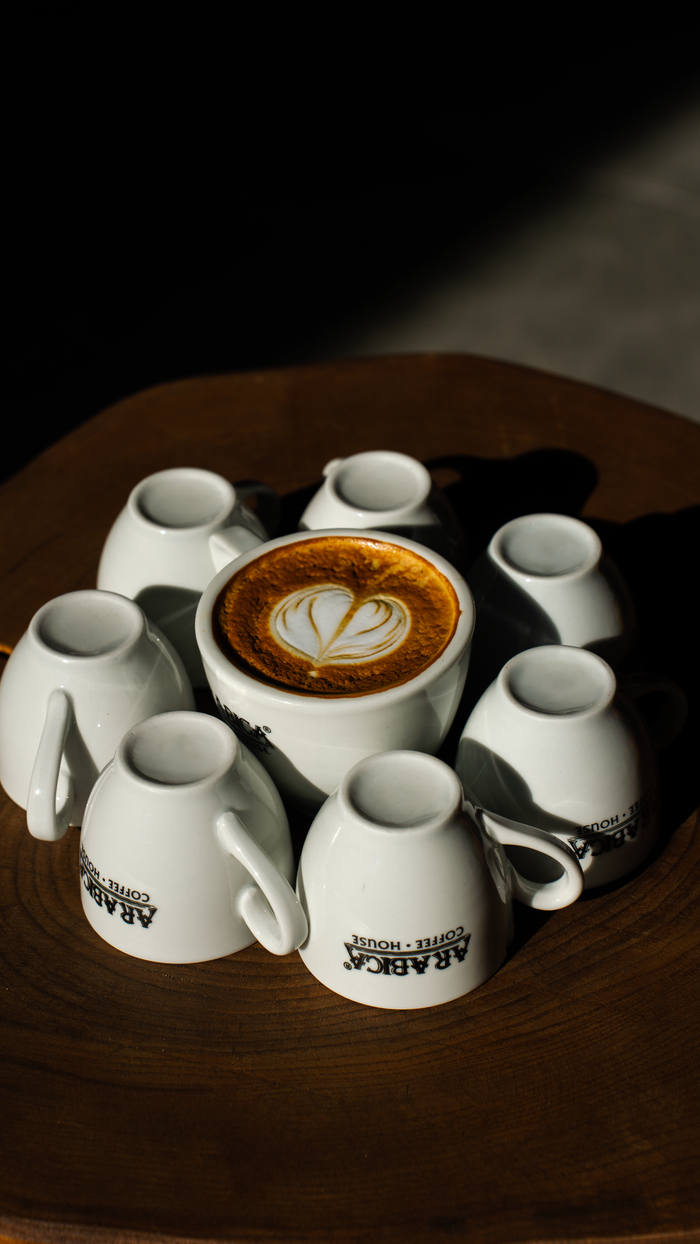 Home Captivating latte art surrounded by white coffee cups on a wooden table under sunlight.