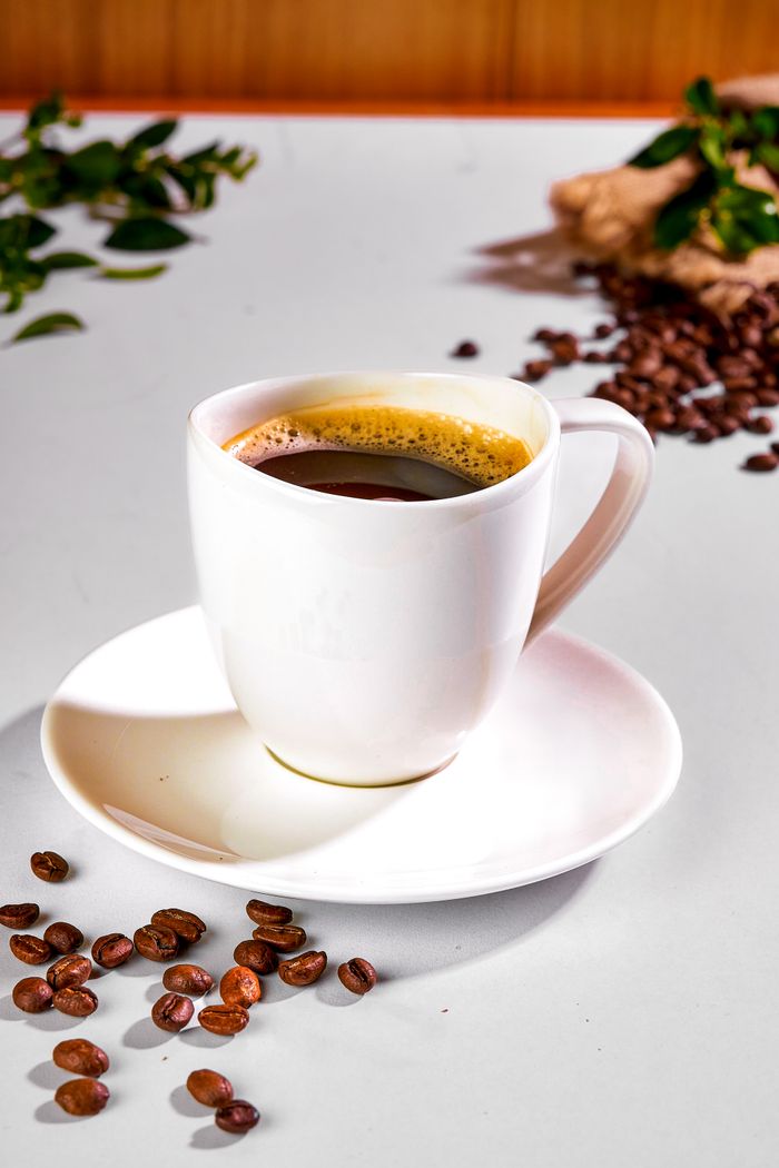 Home Aromatic espresso in a white cup surrounded by coffee beans on a table, ideal for café or coffee-related themes.